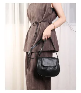Detail view of a stylish black leather crossbody saddle bag worn by a model in casual outfit.