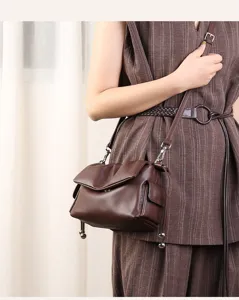 Detail view of brown leather crossbody shoulder bag with unique pleats and metal ball accents.