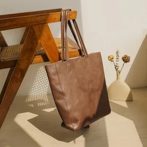 Detail shot of a brown leather tote bag hanging on a wooden chair with dried flowers.