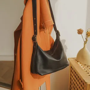 Detailed shot of black leather hobo shoulder bag hanging with orange coat in cozy lifestyle room.