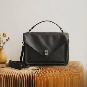 Detailed view of the elegant black leather envelope shoulder bag with metal lock and handle.