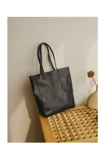 Detail view of a black genuine leather tote bag on a wooden table with minimal decor.