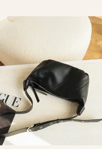 Minimalist black leather dumpling shoulder bag with adjustable strap and zip closure.