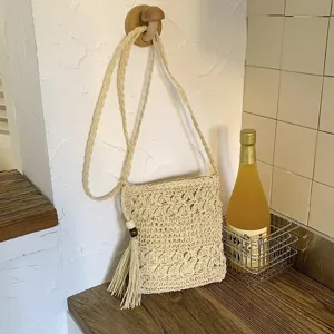 Detalle de bolso cruzado de paja tejida con flecos y cuenta de madera en color beige.