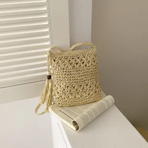 Vista detallada del bolso de hombro de paja tejida con patrón floral calado y borla.