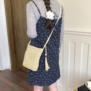 Detalle de bolso cruzado de paja tejida, con material texturizado y un elegante colgante borla.