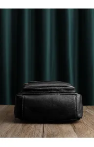 Detailed bottom and side view of black genuine leather backpack showing fine texture and stitching.