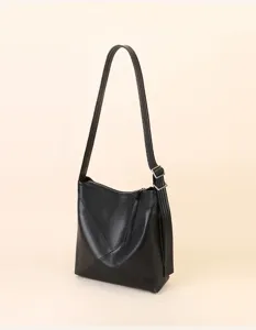 Detail shot of a sleek black leather shoulder bucket bag with adjustable strap and geometric design.