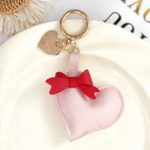Pink leather heart keychain with red bow, cute handbag charm and metal key ring accessory.