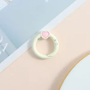 Anillo de resorte verde claro con dije esmaltado de corazón rosa para llavero DIY.