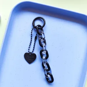 Close-up detail of black and clear acrylic chain key ring with heart pendant for phone case.