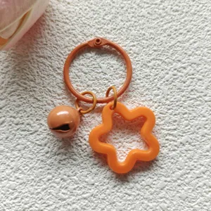 Gedetailleerde close-up van een oranje acryl holle ster en bel sleutelhanger accessoire hangend.