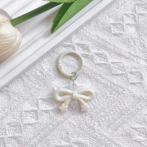 White pearlescent UV bow keychain charm, detailed close-up shot on white lace background.