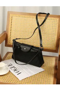 Detailed close-up view of black leather shoulder bag on vintage wooden rattan chair.