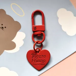 Close-up detail of red metal heart keychain pendant with lobster clasp and engraved text.