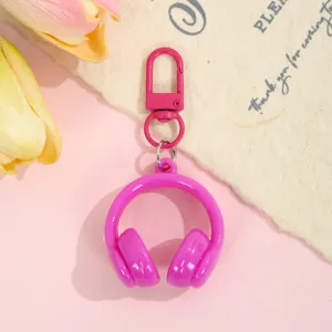 Close-up of cute pink 3D headphone keychain pendant, glossy candy color bag accessory detail.