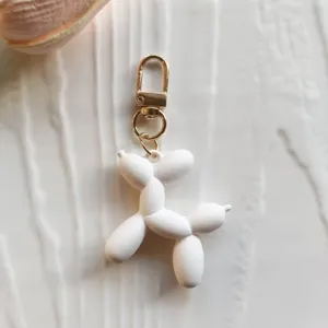 Close up of a cute white rubber balloon dog keychain with gold clasp detail product shot.
