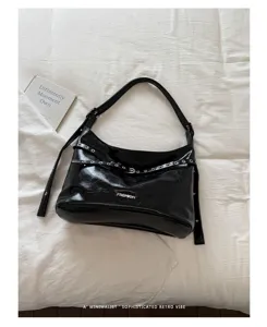 Detailed view of black patent leather shoulder bag with buckle and grommet straps, minimal style.