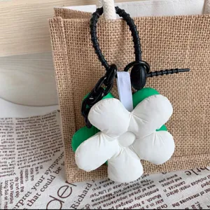 Close-up detail shot of a cute white floral bag charm with black knot and chain pendant.