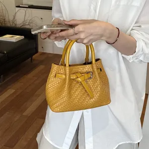 Nahaufnahme der gelben geflochtenen Eimer Tasche mit stilvollem Gürtelknoten für Damen.