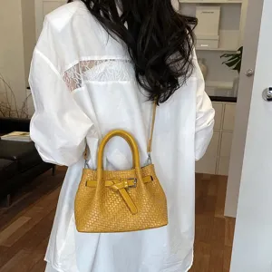 Detaillierte Nahaufnahme einer modischen gelben geflochtenen Eimerhandtasche mit Griff.
