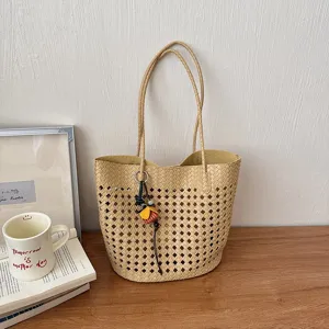 Nahaufnahme der beigen gewebten Loch-Tasche mit Henkeln und Blumen-Anhänger auf Holztisch.