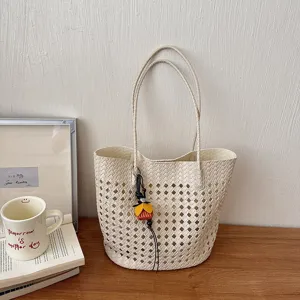 Detailansicht der beigen gewebten, geflochtenen Tasche auf Holztisch mit stilvollen Requisiten.
