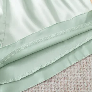 Close up view of women satin pajama shorts hem, smooth light green fabric fine stitching details.