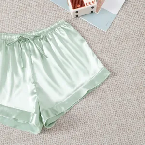 Detail shot of light green satin shorts with drawstring waist and delicate cuff hems.