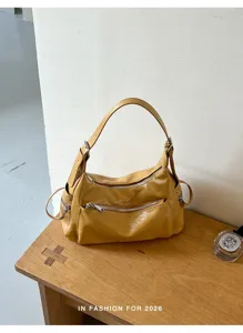 Detail view of a yellow leather shoulder bag with multi zippers on a wooden studio table.