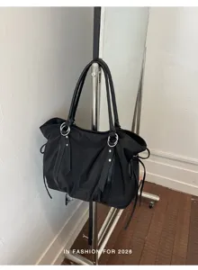 Detail view of black canvas tote bag hanging on metal rack, showing minimalist shoulder design.