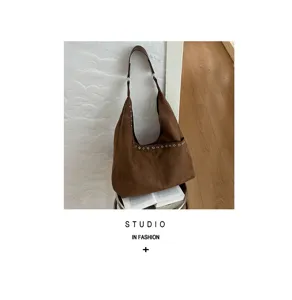 Detailansicht der braunen Wildleder Hobo Umhängetasche mit dekorativen Metallösen und weichem Finish.