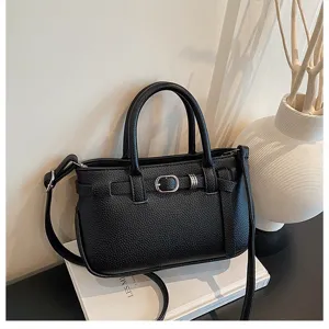 Elegante zwarte lederen handtas met chique gespdetails gepresenteerd op een stijlvol boekprop.