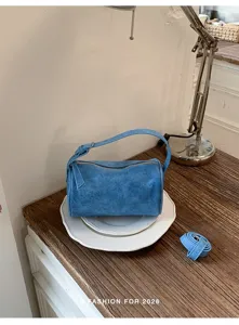 Vista detallada del bolso de hombro cilíndrico de ante azul de tendencia sobre platos.