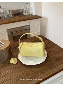 Detalle de bolso bandolera cilíndrico amarillo, elegante bolso de PU en plato blanco.