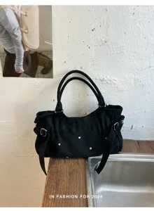 Detailed view of the black canvas shoulder bag with metallic rivets and side buckle straps.