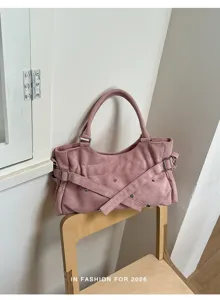Pink suede underarm shoulder bag with metal buckles and rivet details on a wooden chair.