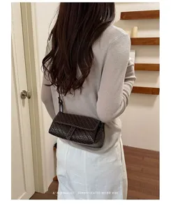 Detailed shot of a dark brown woven leather crossbody bag with flap and slim strap.
