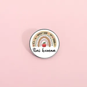 Detailed close-up of a cute metal round pin badge featuring a colorful rainbow and apple design.