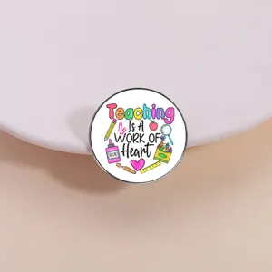 Close-up detail of a round metal brooch badge with teacher theme pattern and lettering.