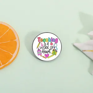 Close up shot of a cute round metal teacher brooch with colorful inspiring typography design.