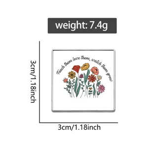 Detail view of a square metal brooch featuring floral patterns and inspirational text.