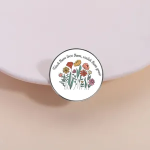 Close-up detail of a cute metal enamel brooch featuring floral illustrations and inspirational quote.