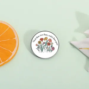 Close-up of a round metal brooch pin, featuring cute floral illustration and quote.