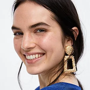 Detailed close-up of textured gold geometric drop earrings worn by model, shining brightly.