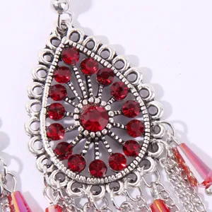 Close-up detail of ethnic drop rhinestone tassel earrings with silver filigree and red stones.