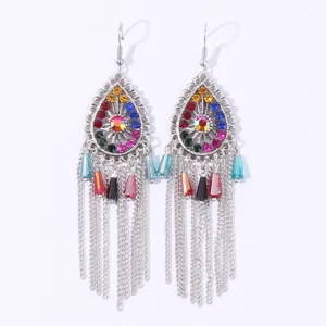Close-up of bohemian drop earrings with colorful rhinestones, metal filigree and dangling chains.