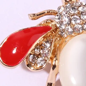 Close-up detail of a cute bee brooch with sparkling rhinestones, red enamel and pearl.