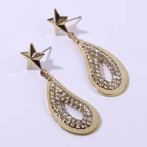 Close-up detail of glittering gold star and pavé rhinestone teardrop dangle earrings.