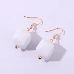 Primo piano dettagliato di orecchini a cubo geometrico bianco con ganci dorati.